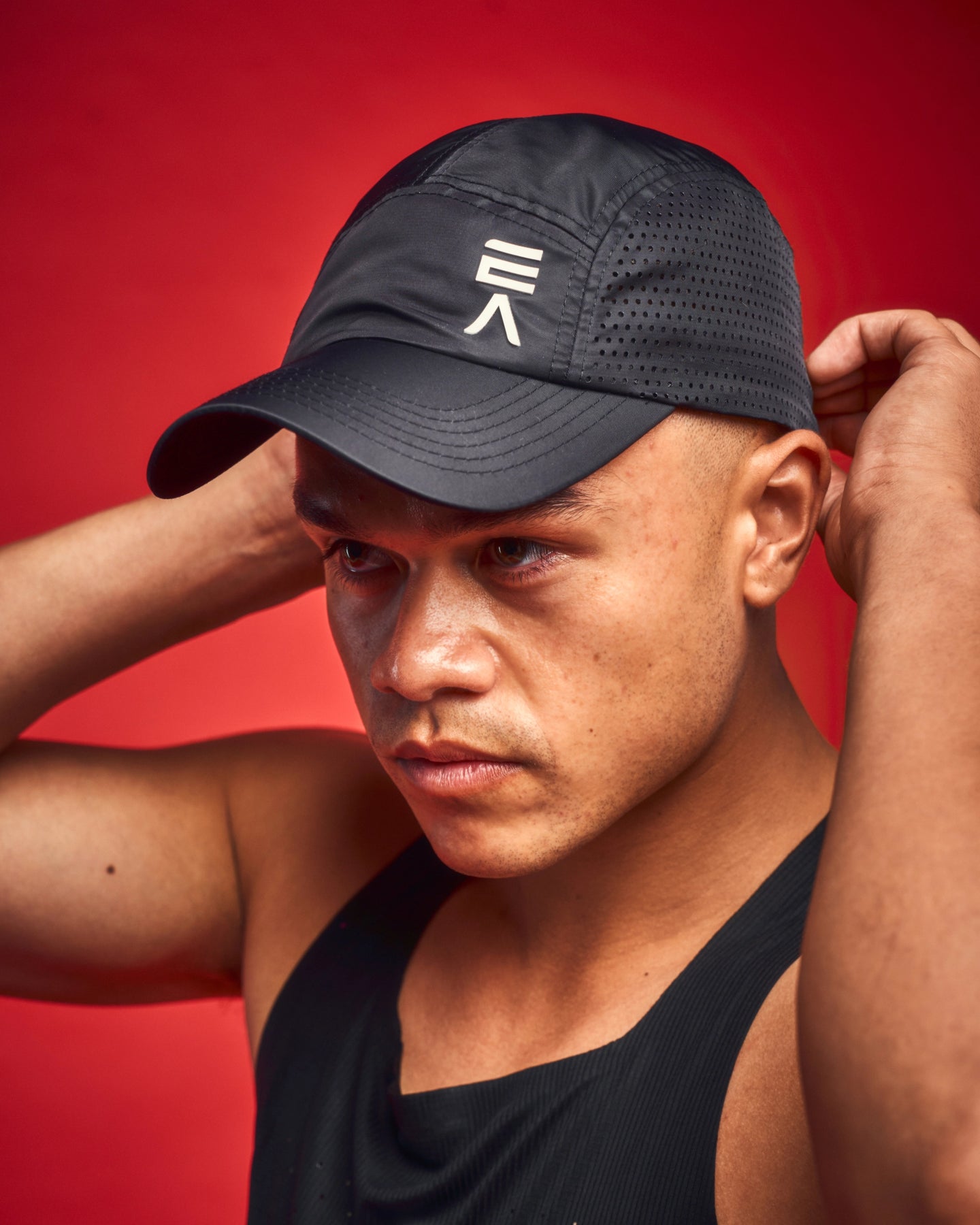 Close-up view of man wearing midnight black EVOActive Core Vented Run Cap with logo visible against a red background