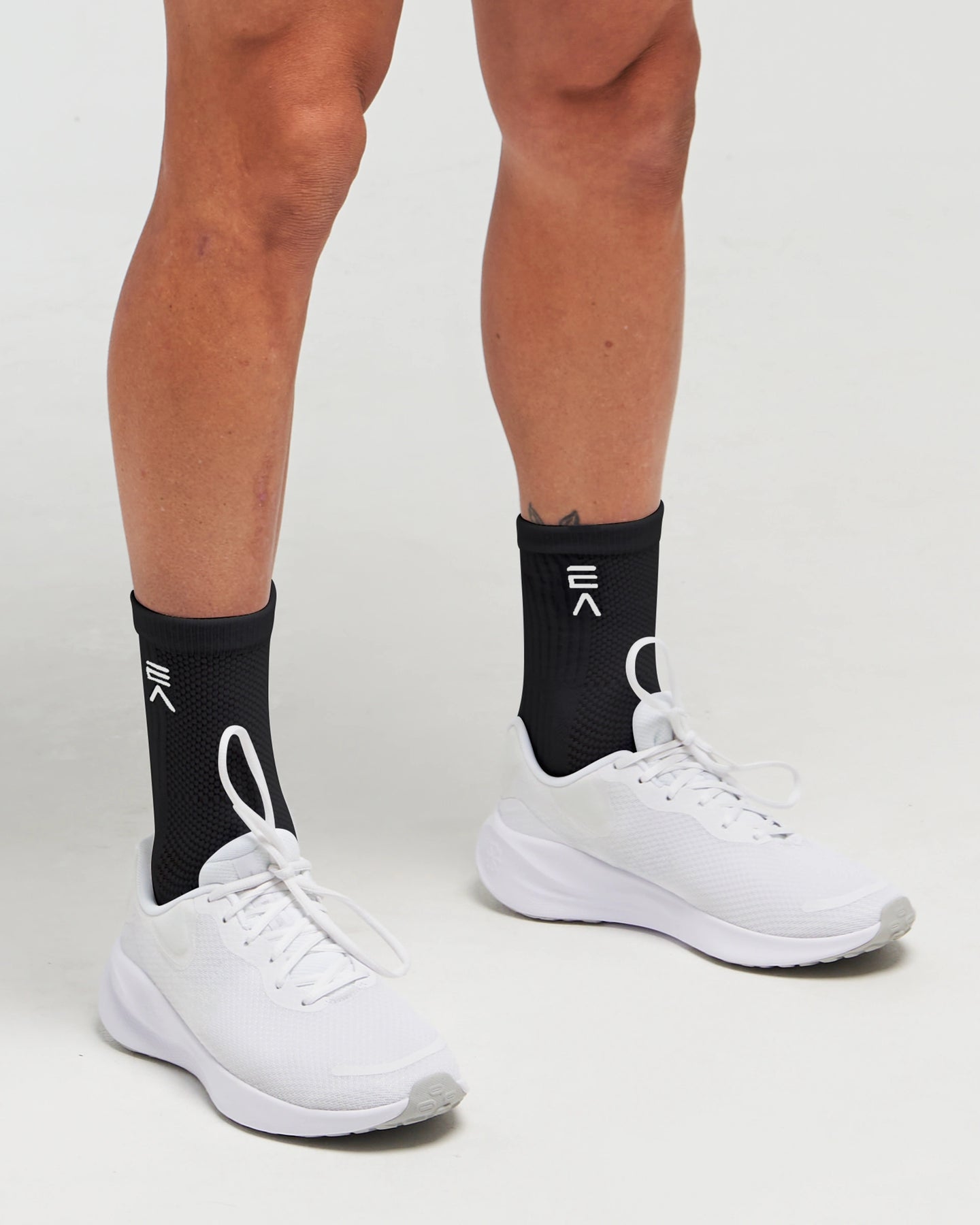 Person wearing midnight black EVOActive Elevate Mid Sock with logo visible, paired with white shoes against a white background