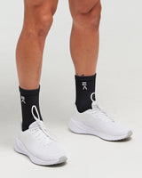 Person wearing midnight black EVOActive Elevate Mid Sock with logo visible, paired with white shoes against a white background