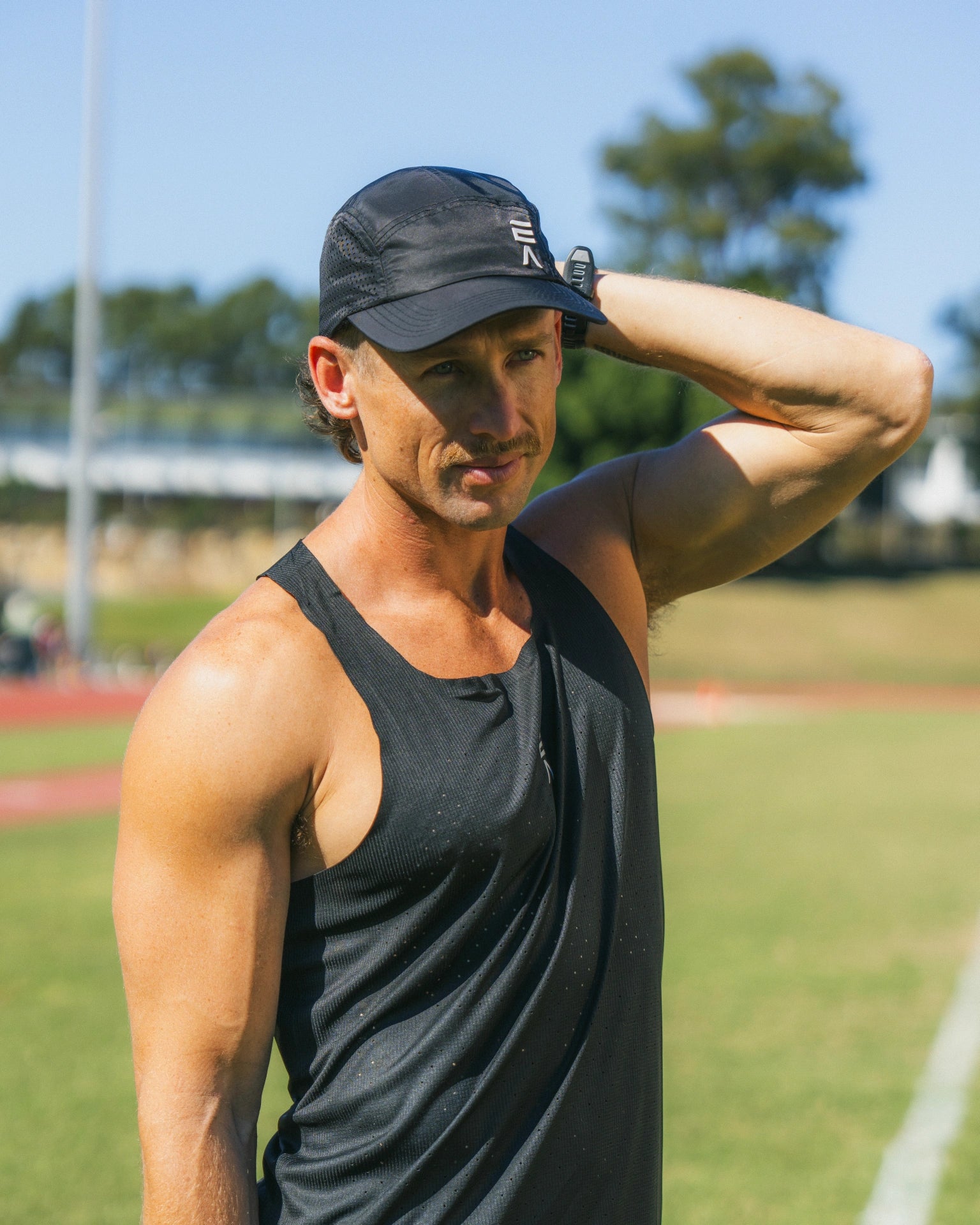 Man wearing midnight black Men’s Aero Singlet standing in a sports field with green open background