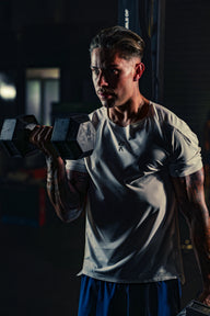 Man wearing EVOActive Men’s Aero Tee lifting a dumbbell in one hand in a gym setting with logo visible