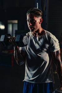 Man wearing EVOActive Men’s Aero Tee lifting a dumbbell in one hand in a gym setting with logo visible