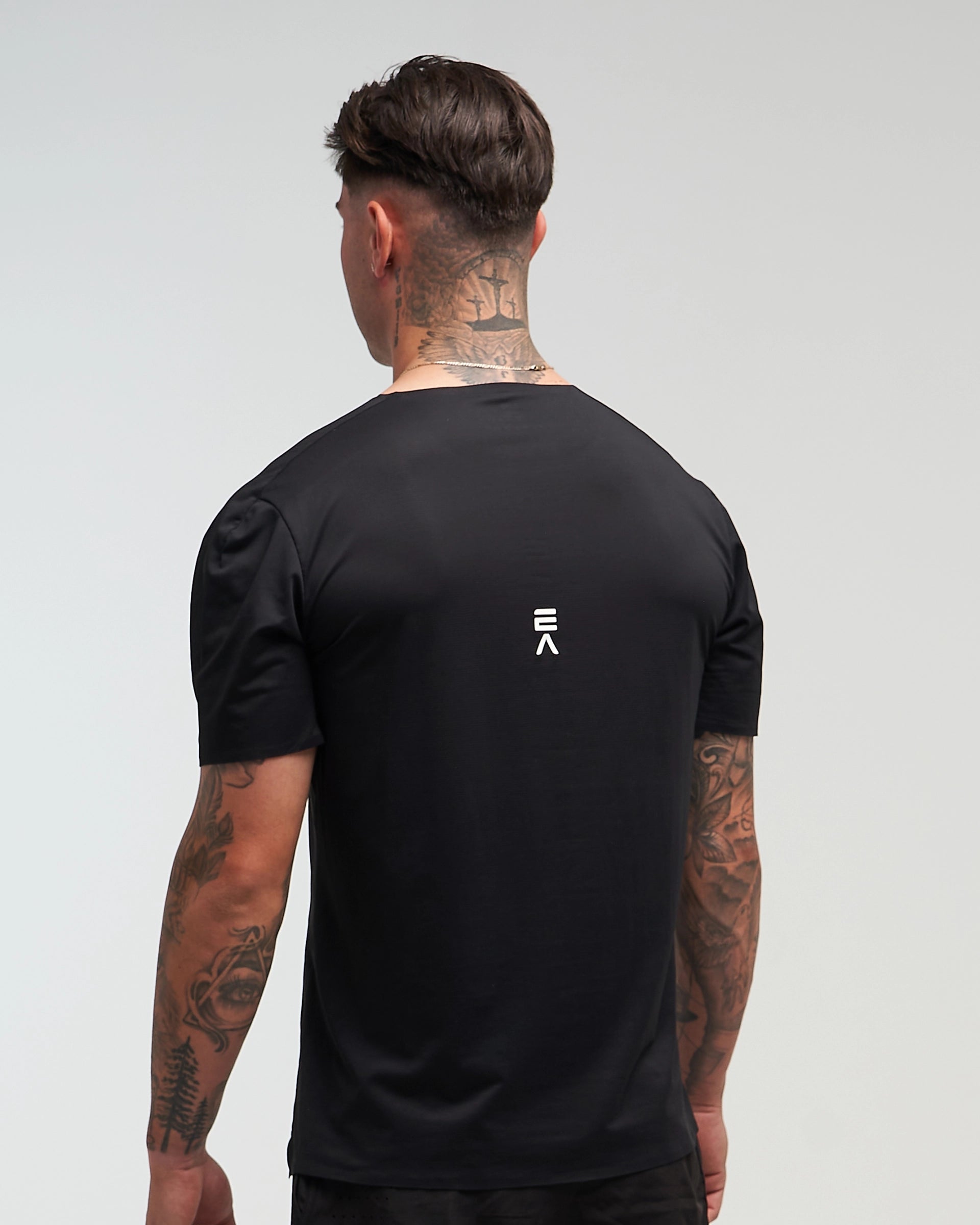 Back view of man wearing midnight black EVOActive Men’s Aero Tee with logo visible against a bright background