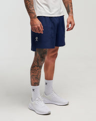 Front view of man wearing eclipse navy EVOActive Men’s FlexMotion Shorts in a slight side pose with logo visible on the shorts against a bright background
