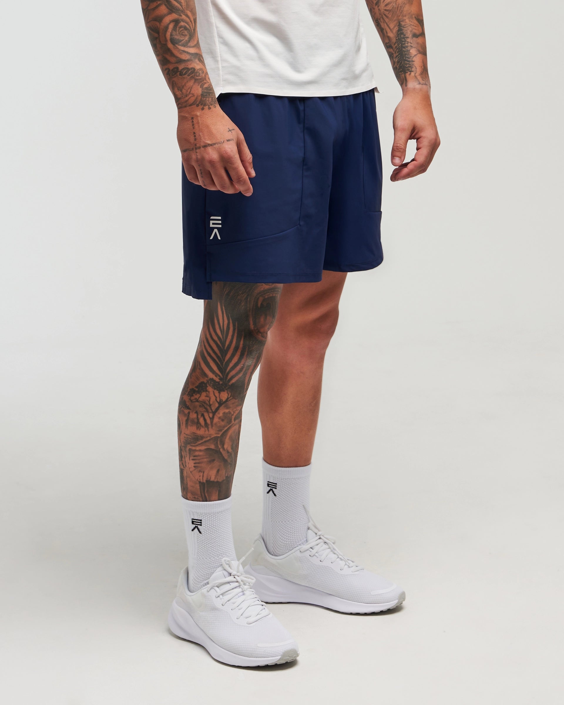 Front view of man wearing eclipse navy EVOActive Men’s FlexMotion Shorts in a slight side pose with logo visible on the shorts against a bright background