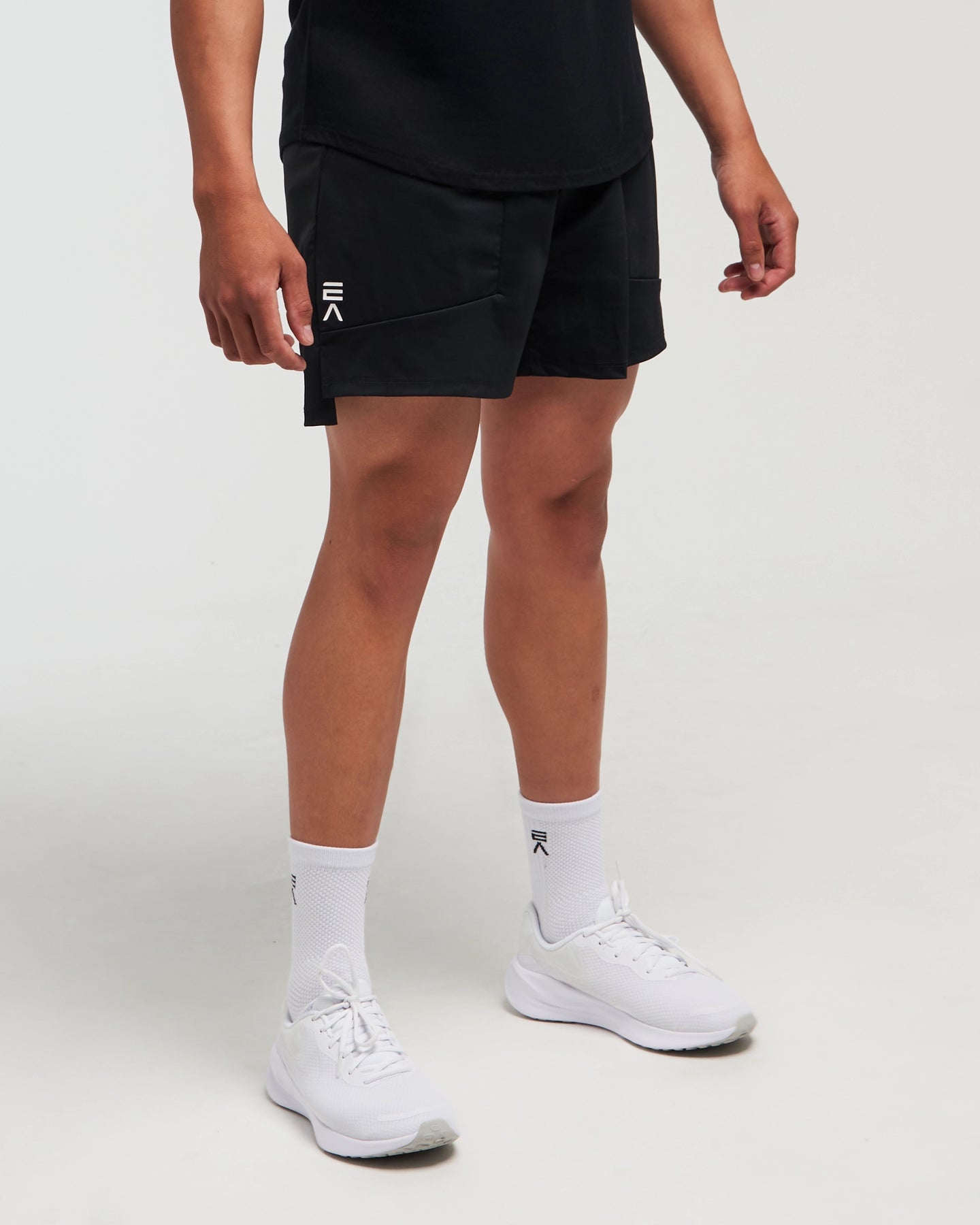 Lower half view of man wearing midnight black EVOActive Men’s FlexMotion Shorts in a slight side pose with front  and logo visible