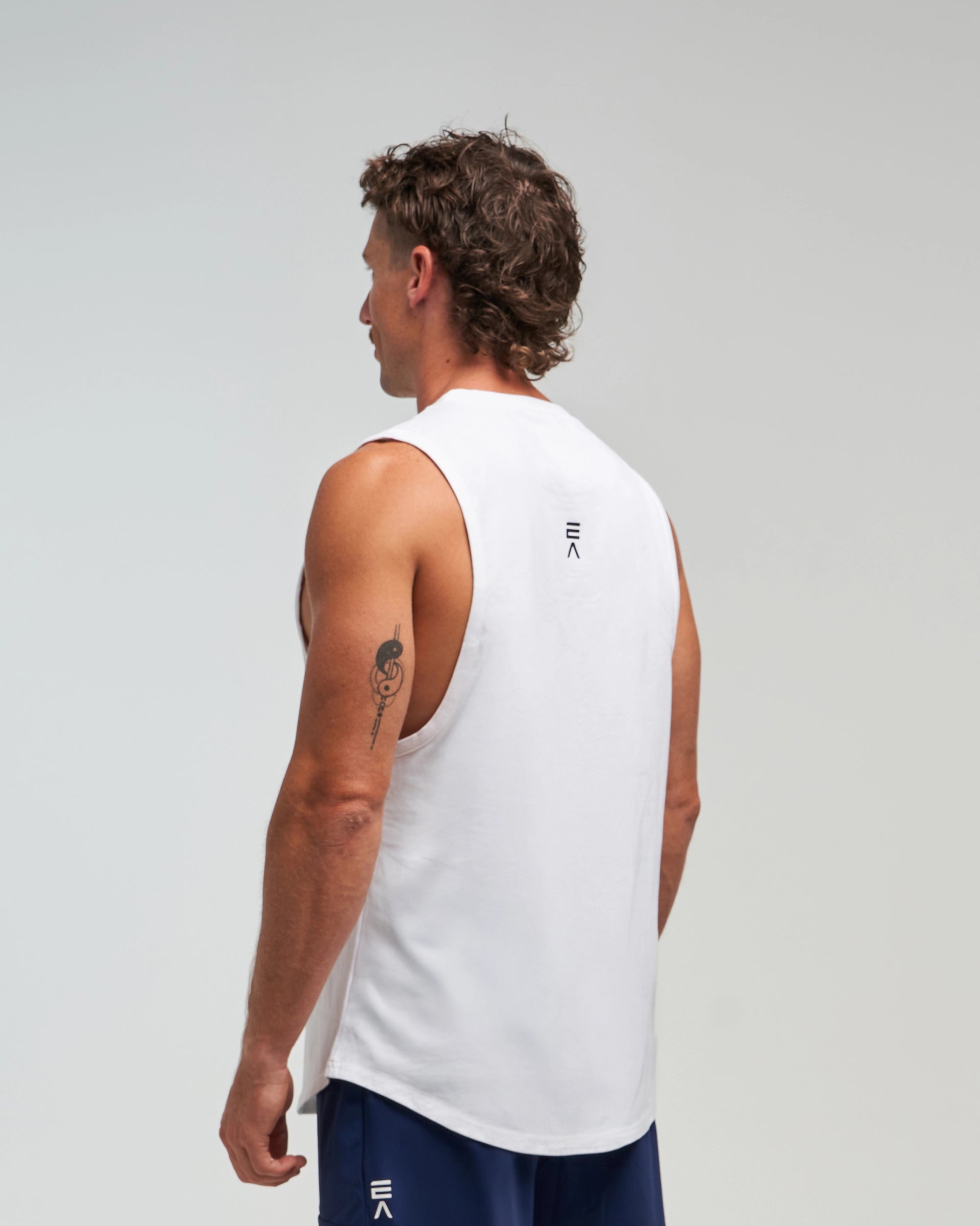 Half-body back view of man wearing Evo Ice white EVOActive Men’s Flex Singlet in a slight side pose with logo visible