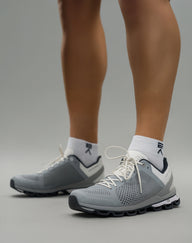 Person wearing Evo Ice white EVOActive Sprint Low Sock with logo visible, paired with grey shoes against a bright studio background