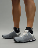 Person wearing midnight black EVOActive Sprint Low Sock with logo visible, paired with grey shoes against a bright studio background