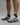 Person wearing midnight black EVOActive Sprint Low Sock with logo visible, paired with grey shoes against a bright studio background
