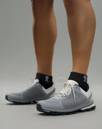 Person wearing midnight black EVOActive Sprint Low Sock with logo visible, paired with grey shoes against a bright studio background