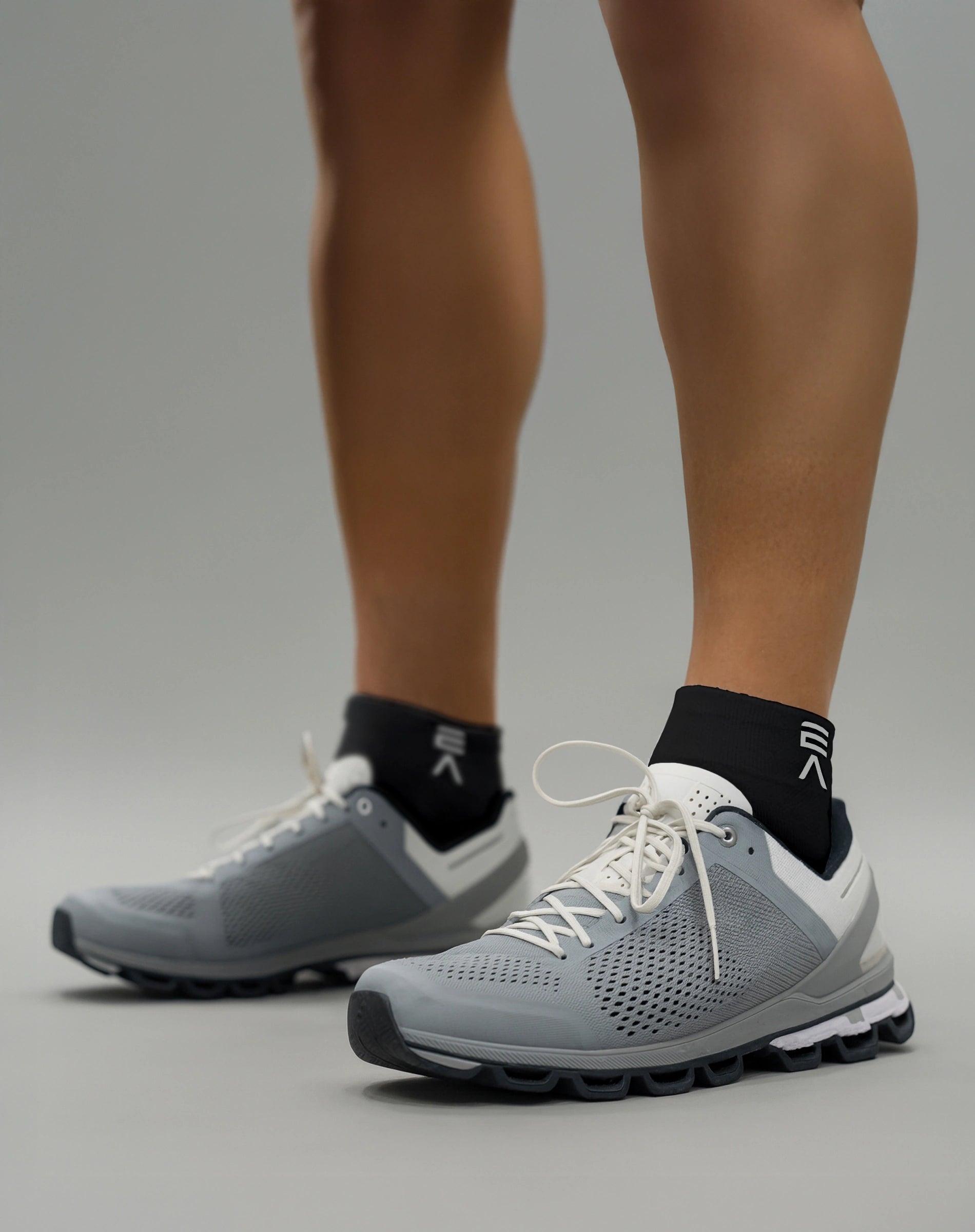 Person wearing midnight black EVOActive Sprint Low Sock with logo visible, paired with grey shoes against a bright studio background