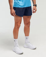 Half-body view of man wearing deep blue EVOActive Unisex Aero Run Short with logo visible on the shorts against a bright background