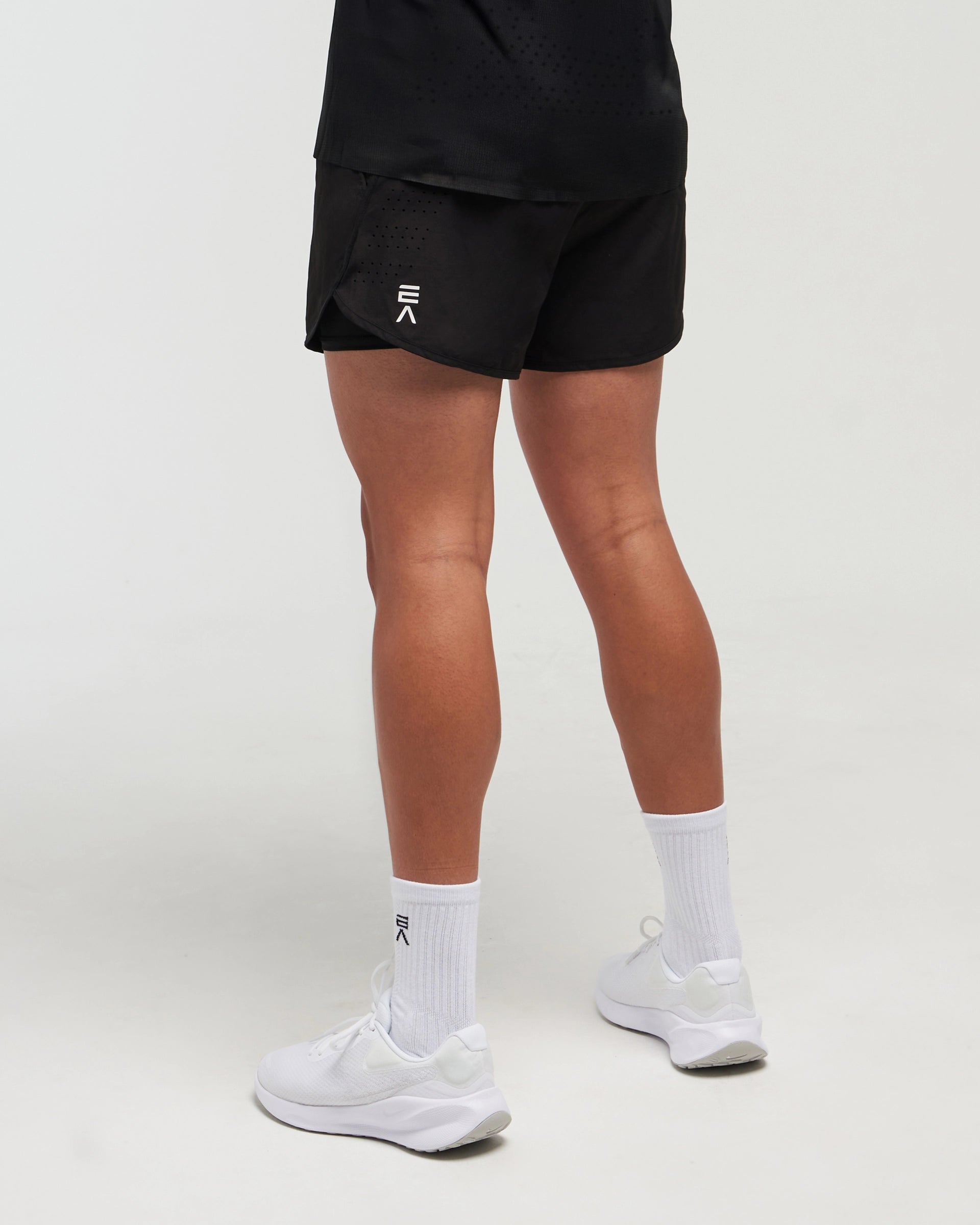 Half-body slight side pose with back visible of man wearing midnight black EVOActive Unisex Aero Run Short with logo visible on the shorts against a bright background