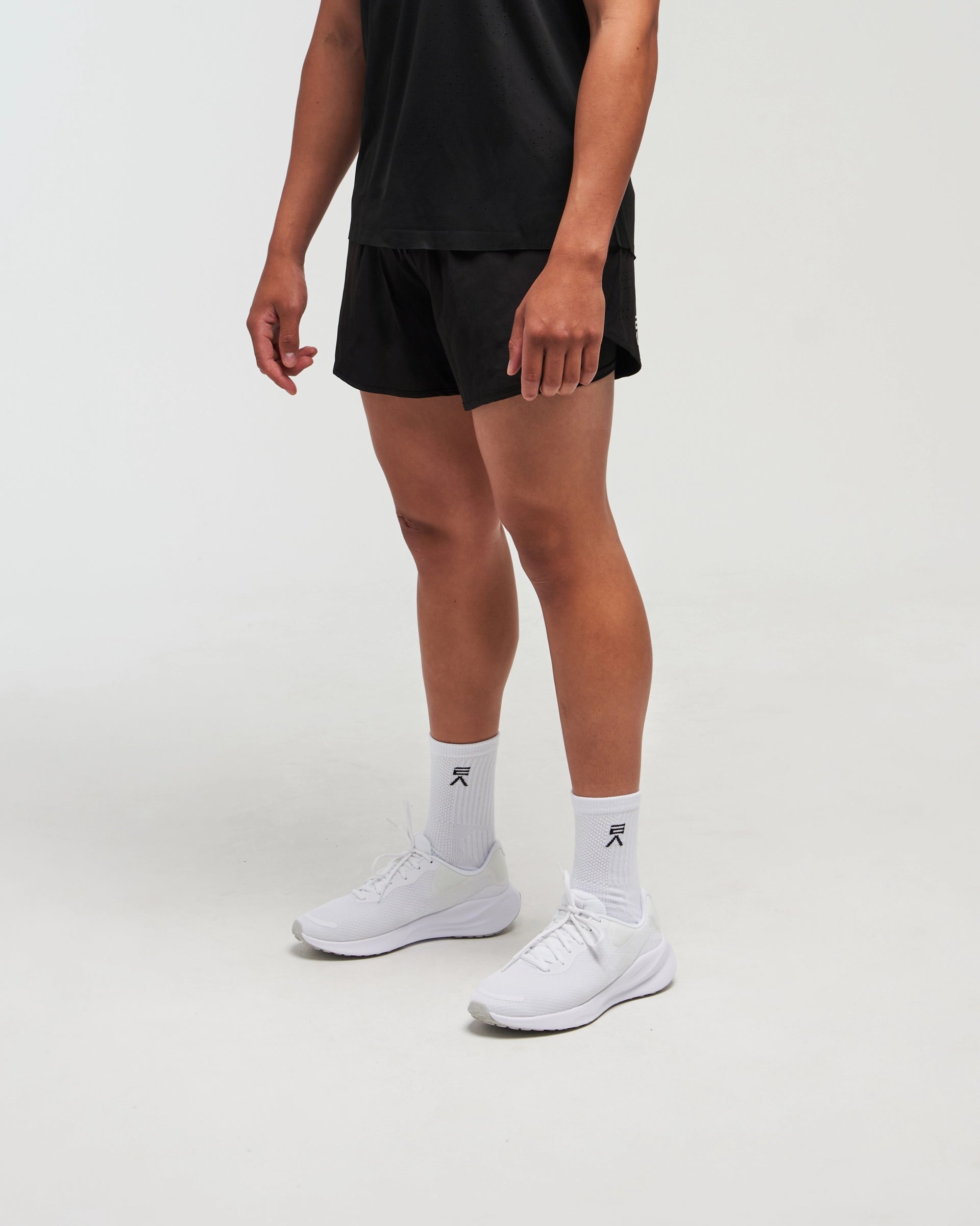 Half-body side pose with front visible of man wearing midnight black Unisex Aero Run Short against a bright background