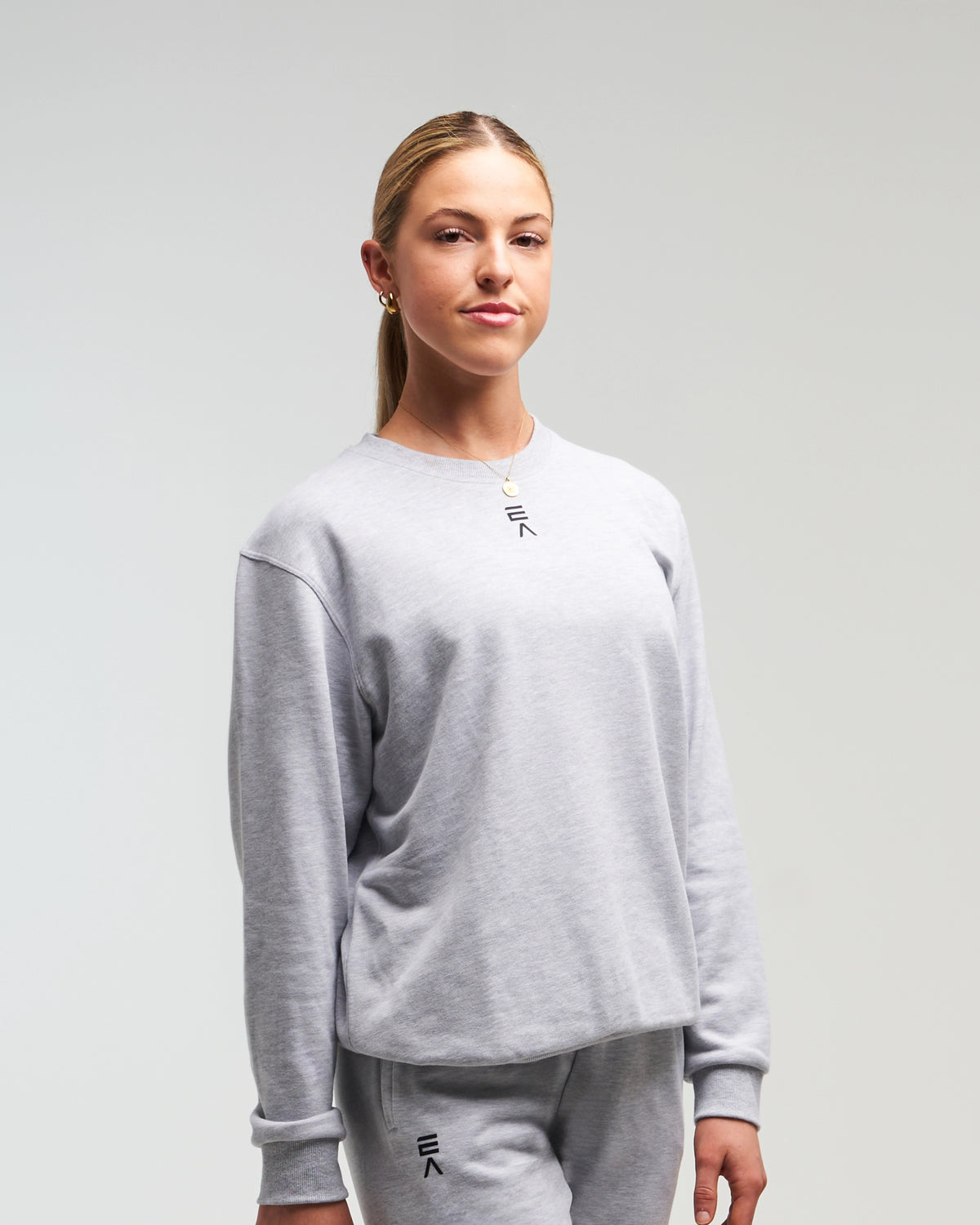 Front view of woman wearing clouded grey EVOActive Unisex Classic LS Crew Neck Tee with logo visible against a bright background