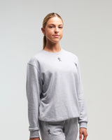 Front view of woman wearing clouded grey EVOActive Unisex Classic LS Crew Neck Tee with logo visible against a bright background