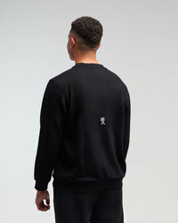 Back view of man wearing midnight black EVOActive Unisex Classic LS Crew Neck Tee with logo visible on the garment against a bright background