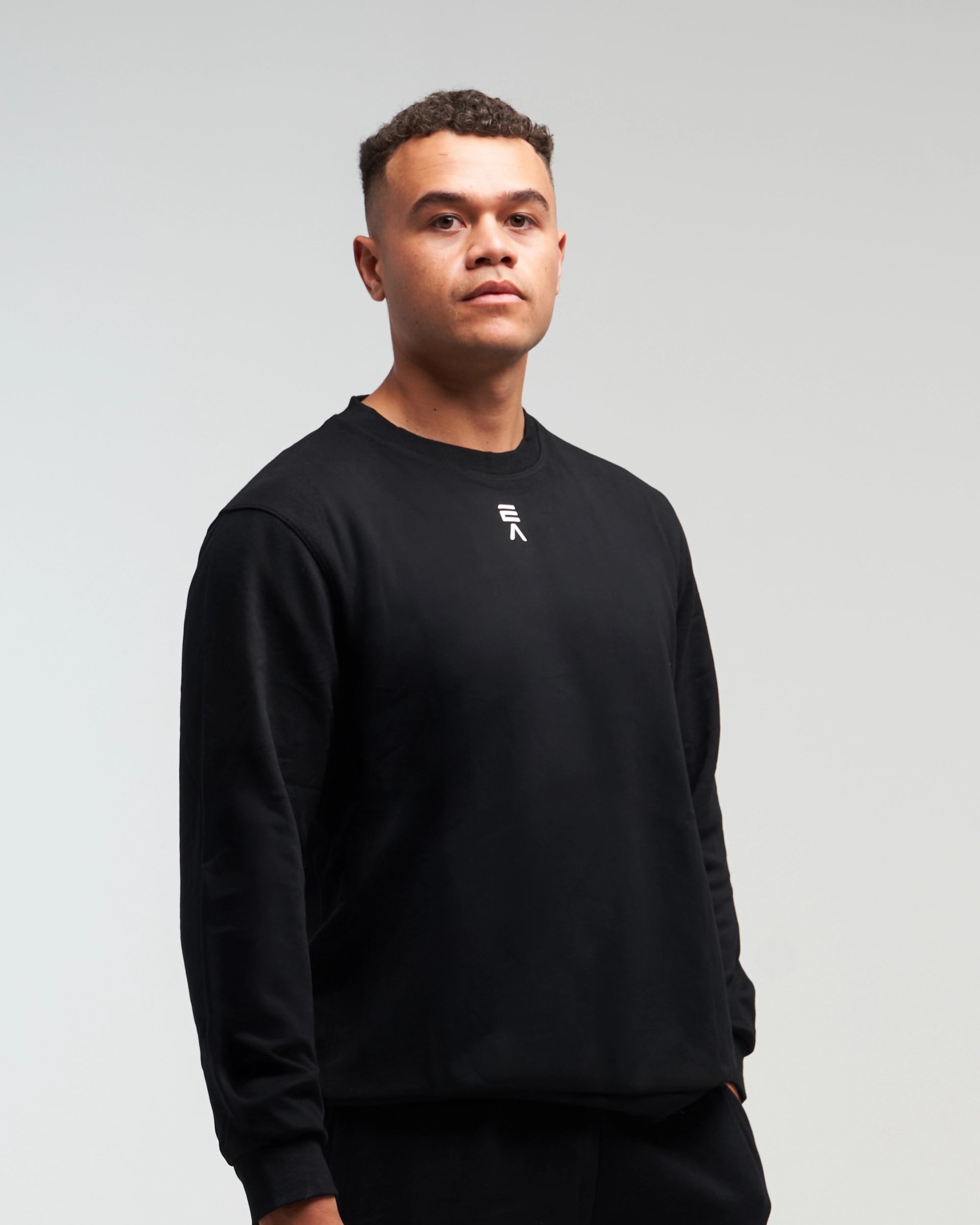 Front view of man wearing midnight black EVOActive Unisex Classic LS Crew Neck Tee with logo visible on the garment against a bright background