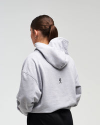 Back view of woman in a slight side pose wearing clouded grey EVOActive Unisex Classic Pullover Hoody with logo visible on the garment against a bright background