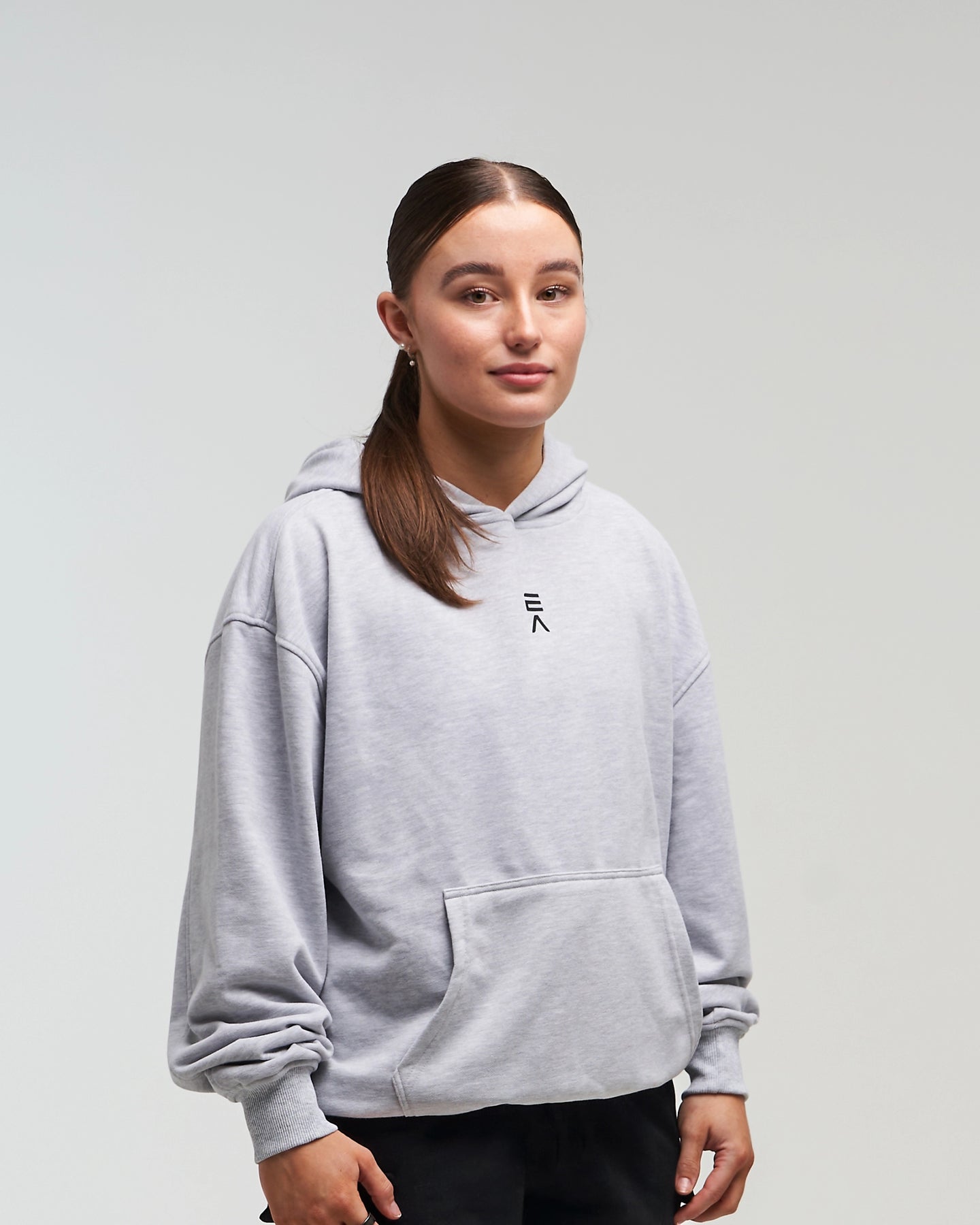 Front view of woman in a slight side pose wearing clouded grey EVOActive Unisex Classic Pullover Hoody with logo visible on the garment against a bright background