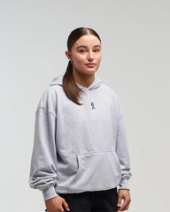 Front view of woman in a slight side pose wearing clouded grey EVOActive Unisex Classic Pullover Hoody with logo visible on the garment against a bright background