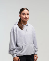 Front view of woman in a slight side pose wearing clouded grey EVOActive Unisex Classic Pullover Hoody with logo visible on the garment against a bright background