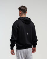 Back view of man wearing midnight black EVOActive Unisex Classic Pullover Hoody with logo visible on the garment against a bright background
