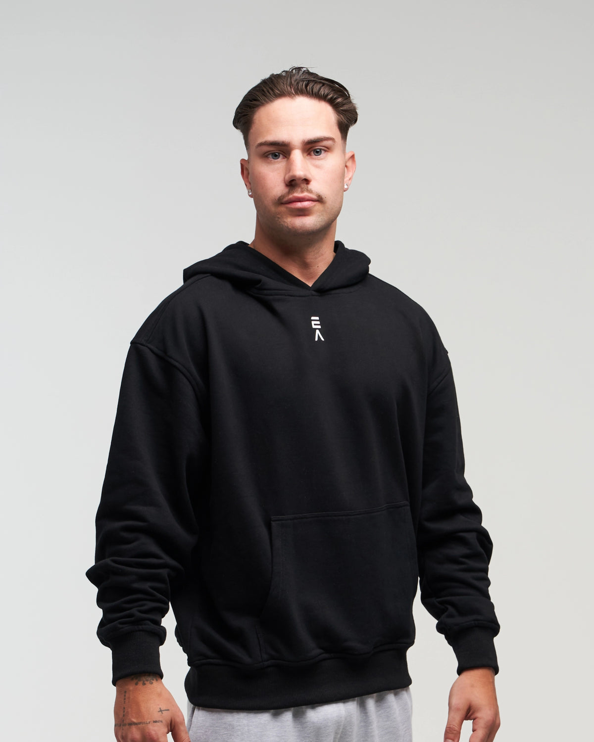 Front view of man in a slight side pose wearing midnight black EVOActive Unisex Classic Pullover Hoody against a bright background