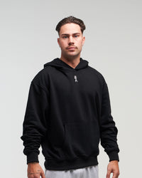 Front view of man in a slight side pose wearing midnight black EVOActive Unisex Classic Pullover Hoody against a bright background