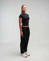 Full body view of woman wearing midnight black EVOActive Unisex Classic Straight-Leg Jogger Pant with logo visible on the leggings against a bright background