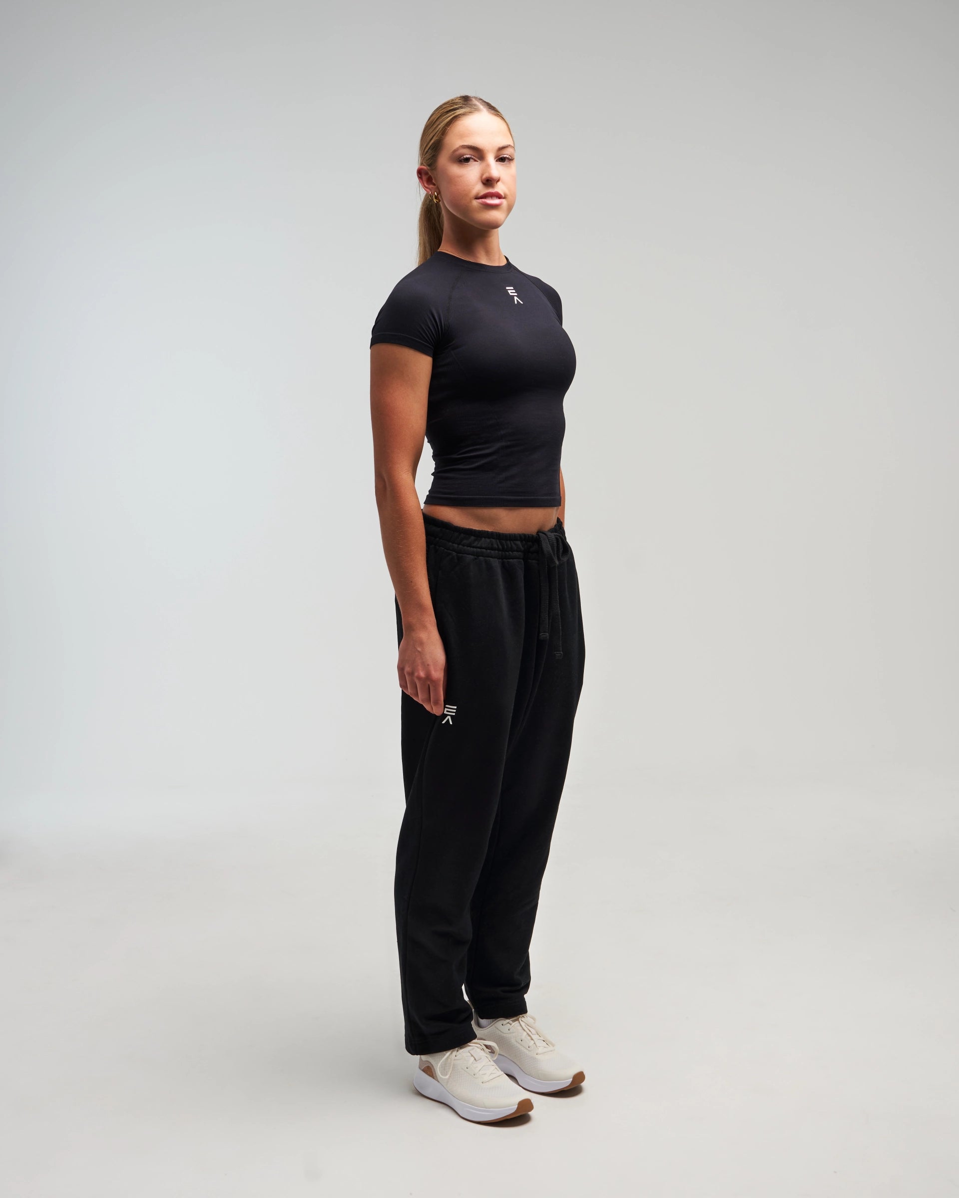 Full body view of woman wearing midnight black EVOActive Unisex Classic Straight-Leg Jogger Pant with logo visible on the leggings against a bright background