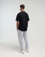 Full body back view of man in a slight side pose wearing midnight black EVOActive Unisex Classic Tee with logo visible against a bright plain background