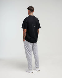 Full body back view of man in a slight side pose wearing midnight black EVOActive Unisex Classic Tee with logo visible against a bright plain background