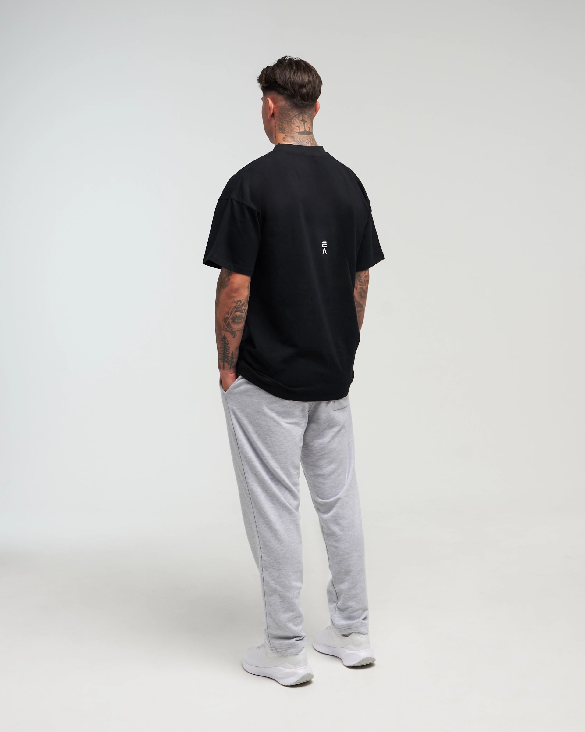 Full body back view of man in a slight side pose wearing midnight black EVOActive Unisex Classic Tee with logo visible against a bright plain background