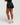 Back view showing body from upper back to feet of woman wearing midnight black EVOActive Women’s CoreRacer Short with logo visible against bright background