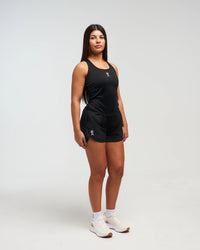 Full body front view of woman wearing midnight black EVOActive Women’s CoreRacer Short with logo visible against a bright background