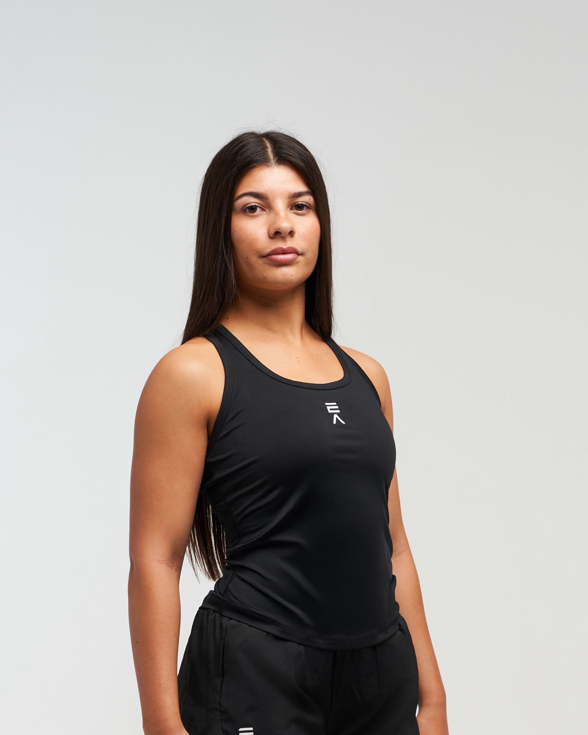 Woman wearing black EVOActive Women’s CoreRacer Singlet sleeveless sports top with logo against bright background