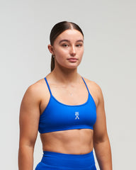 Front view of woman wearing storm blue EVOActive Women’s Elevate Open Back Sports Bra in a slight side pose with logo visible