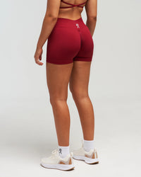 Back view of woman wearing red EVOActive Women’s Elevate Short in a slight side pose with logo visible