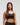 Close-up front view of woman wearing midnight black EVOActive Women’s Flex Sports Bra with logo visible against bright background
