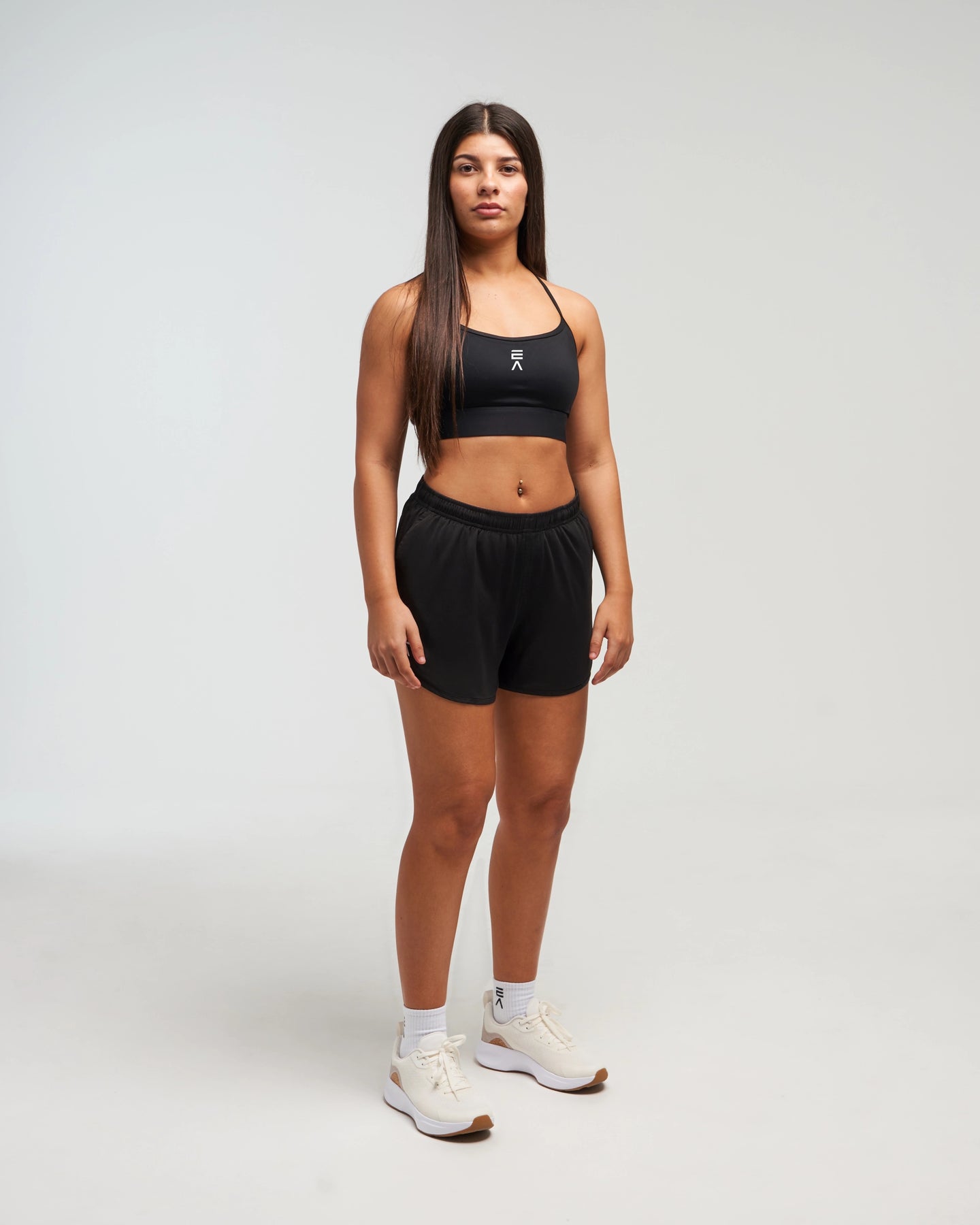 Front view of woman wearing midnight black EVOActive Women’s Flex Sports Bra in a slight side pose with logo visible against bright background