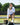Woman sitting on a bench wearing Evo Ice white EVOActive Women’s Horizon Jacket, sipping a beverage with dog nearby and logo visible against trees and open field background