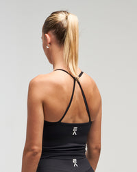 Back view of woman wearing black EVOActive Women’s Motion Open Back Singlet with logo visible against bright background
