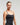 Front half body view of woman wearing black EVOActive Women’s Motion Open Back Singlet in a slight side pose with logo visible against bright background