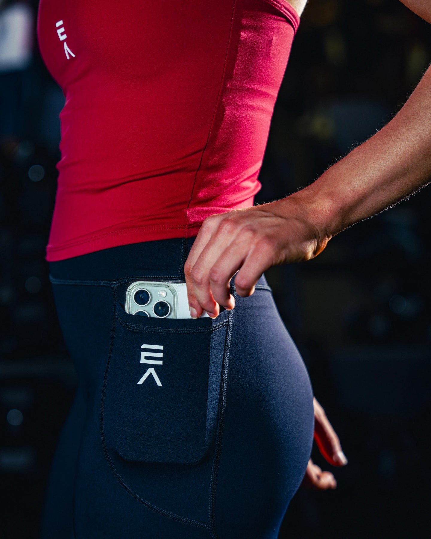 Side view of woman wearing midnight black EVOActive Women’s Motion Pocket Leggings with logo visible and mobile in pocket