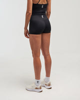 Back view of woman wearing midnight black EVOActive Women’s Motion Short in a slight side pose with logo visible against bright background